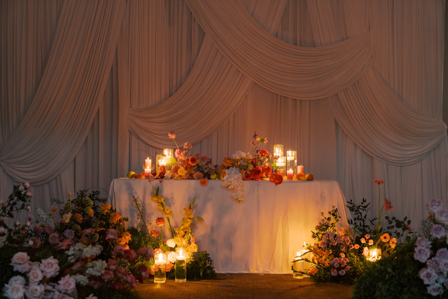 Tavolo nuziale decorato con composizioni floreali arancioni e candele accese.