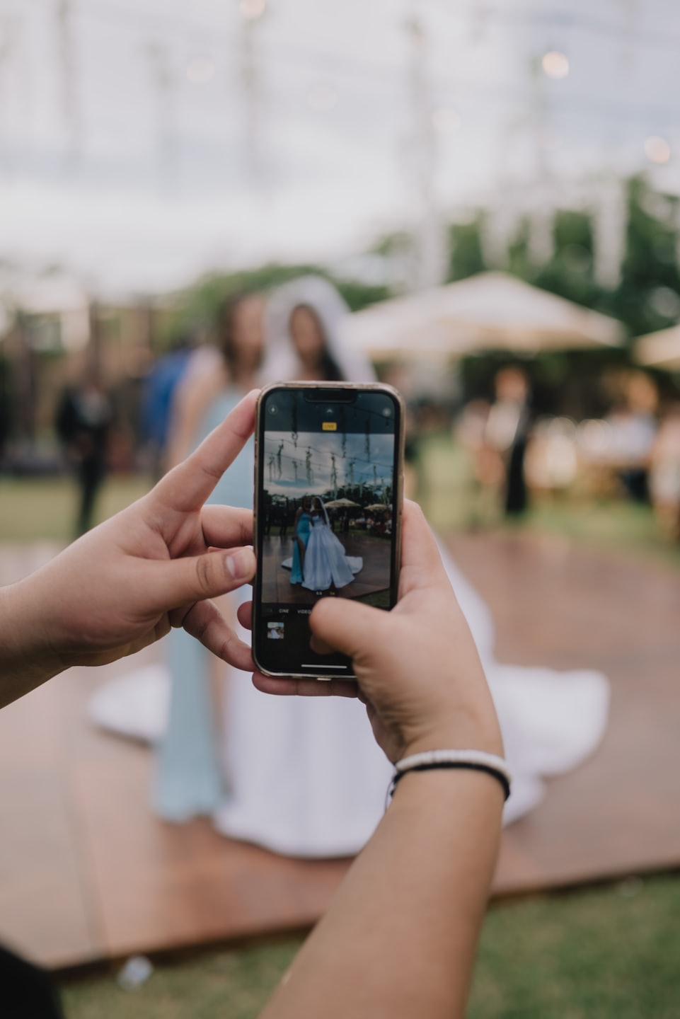 Mani che tengono uno smartphone dorato per fotografare una sposa e una damigella d'onore.